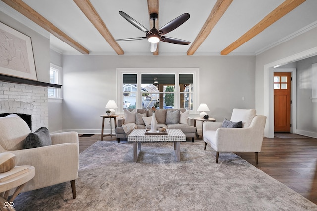 living area featuring wood finished floors, baseboards, beamed ceiling, ceiling fan, and a brick fireplace