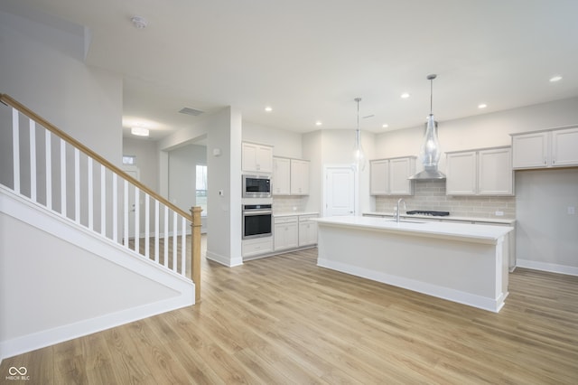 kitchen with light wood finished floors, backsplash, light countertops, appliances with stainless steel finishes, and a sink