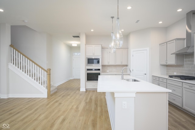 kitchen featuring visible vents, a sink, stainless steel appliances, light wood-style floors, and wall chimney range hood