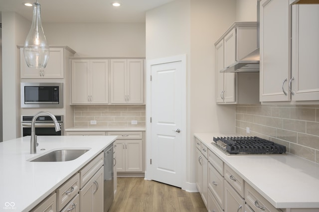 kitchen featuring a sink, light wood-style floors, appliances with stainless steel finishes, wall chimney exhaust hood, and light countertops