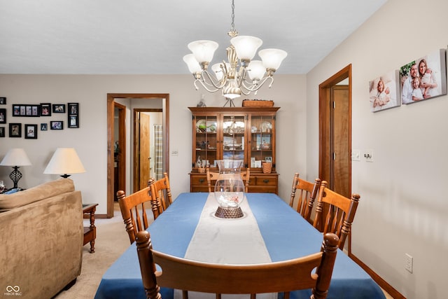 dining room with light carpet, a notable chandelier, and baseboards