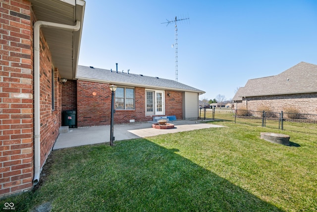 back of house with brick siding, roof with shingles, a fenced backyard, a yard, and a patio