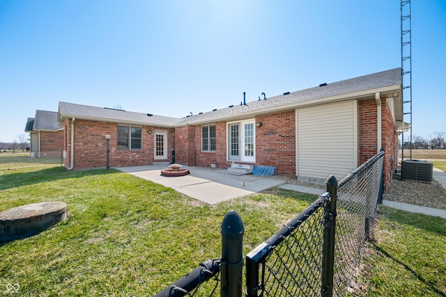 rear view of property featuring a lawn, fence, cooling unit, brick siding, and a patio area