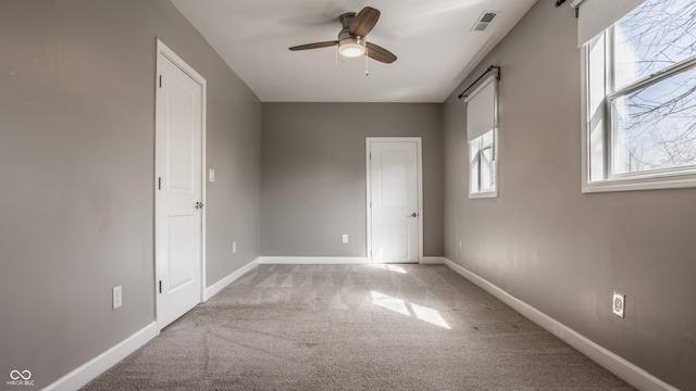 unfurnished bedroom with visible vents, ceiling fan, baseboards, a barn door, and light carpet