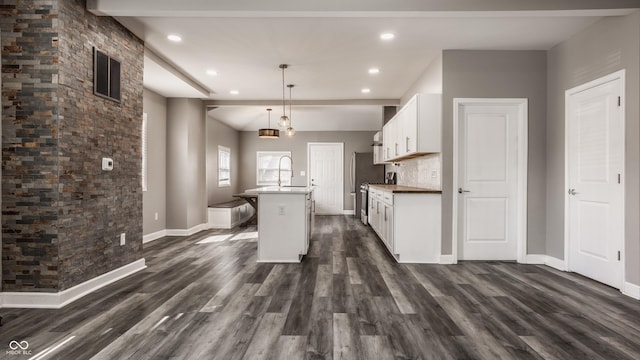 kitchen with dark wood finished floors, a center island with sink, visible vents, and white cabinetry