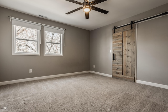 empty room with visible vents, a barn door, carpet floors, baseboards, and ceiling fan