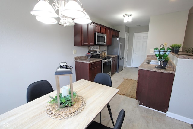 kitchen with reddish brown cabinets, baseboards, a chandelier, appliances with stainless steel finishes, and a sink