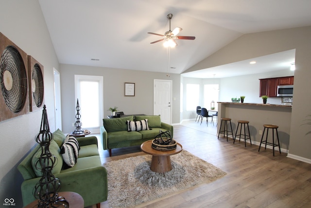 living area featuring visible vents, baseboards, light wood-type flooring, lofted ceiling, and a ceiling fan