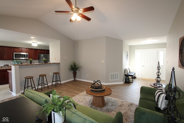 living room with visible vents, baseboards, ceiling fan, vaulted ceiling, and light wood-style flooring