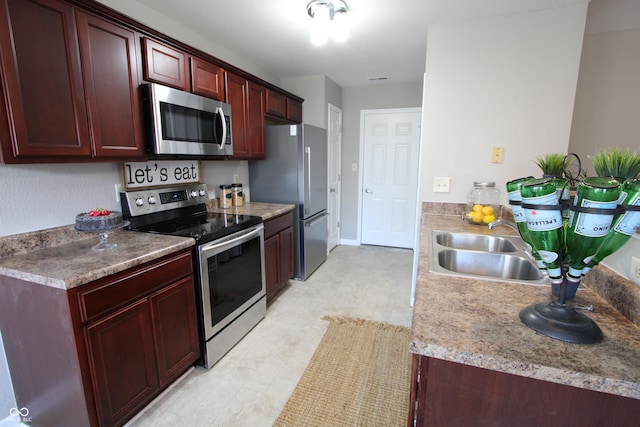 kitchen with reddish brown cabinets, baseboards, appliances with stainless steel finishes, and a sink