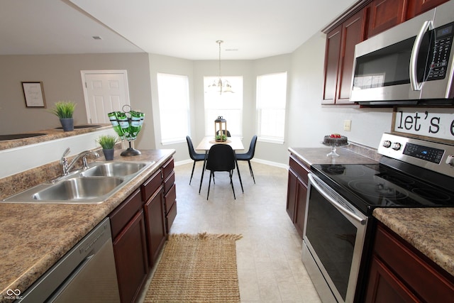 kitchen with baseboards, a sink, stainless steel appliances, a notable chandelier, and reddish brown cabinets