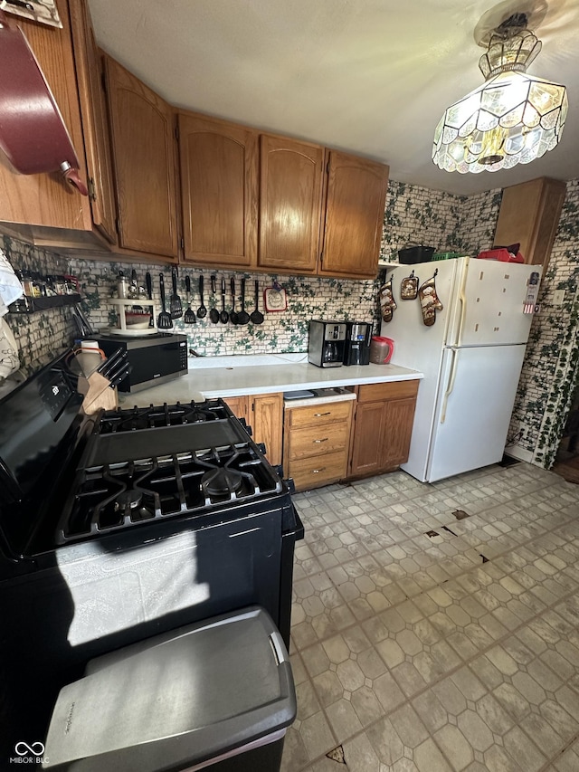 kitchen featuring black gas stove, brown cabinets, light countertops, and freestanding refrigerator