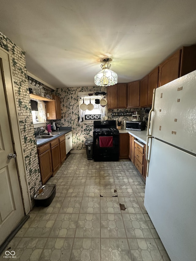 kitchen with stainless steel microwave, brown cabinets, freestanding refrigerator, gas stove, and a sink