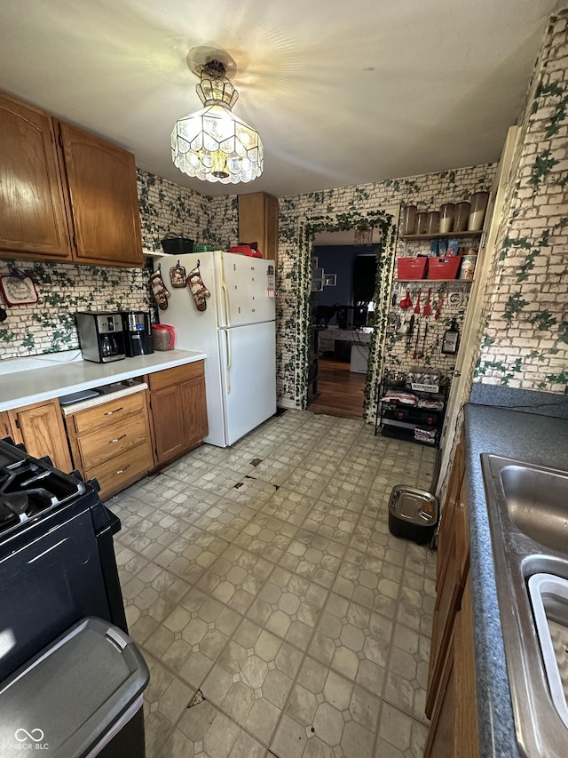 kitchen featuring light floors, gas stove, freestanding refrigerator, light countertops, and brown cabinets