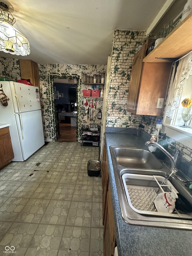 kitchen featuring a sink, brown cabinets, dark countertops, and freestanding refrigerator