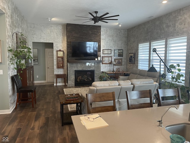 living area with dark wood finished floors, a ceiling fan, baseboards, and a fireplace