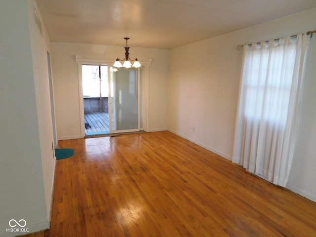 spare room with a chandelier, visible vents, baseboards, and wood finished floors