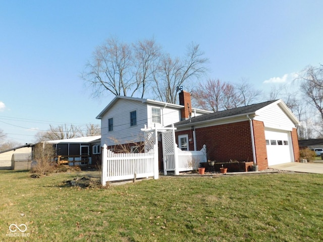 back of property featuring driveway, an attached garage, a chimney, a lawn, and brick siding