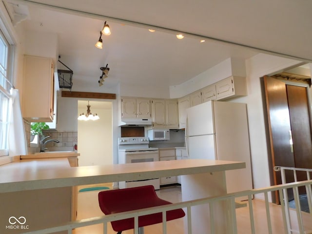 kitchen featuring white appliances, a peninsula, a sink, under cabinet range hood, and tasteful backsplash