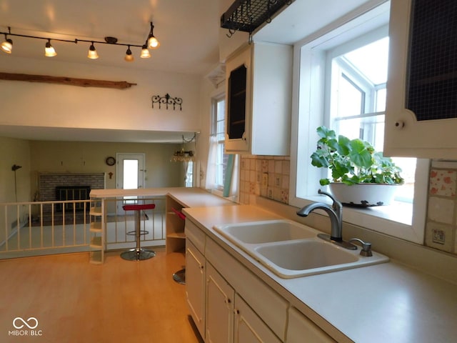 kitchen featuring light wood-style flooring, a sink, white cabinets, light countertops, and decorative backsplash