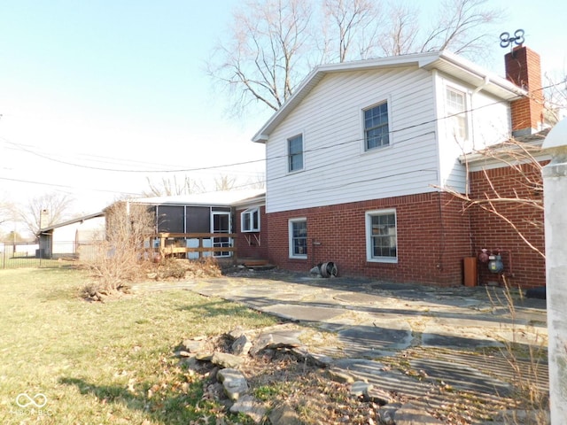 back of house featuring brick siding, a lawn, a chimney, and a sunroom