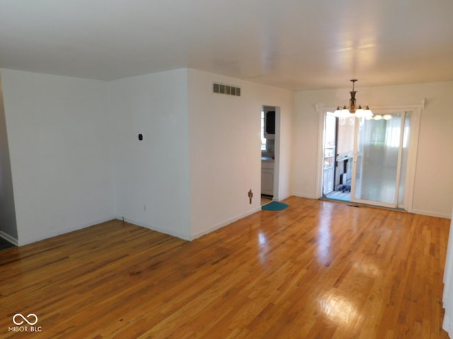 unfurnished room with visible vents, a notable chandelier, and light wood-style flooring