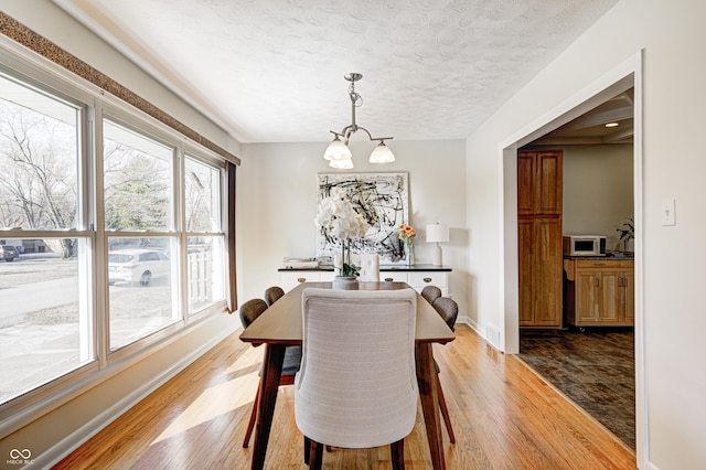 dining space featuring a textured ceiling, hardwood / wood-style flooring, baseboards, and a chandelier