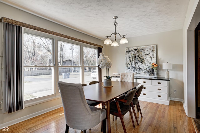 dining space featuring a chandelier, a textured ceiling, light wood-type flooring, and baseboards