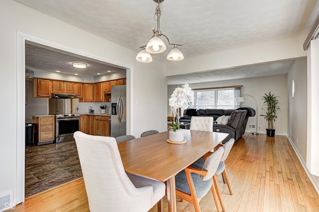 dining area featuring light wood finished floors, visible vents, a textured ceiling, and baseboards