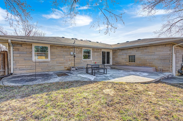 back of house featuring stone siding, a lawn, a patio, and fence