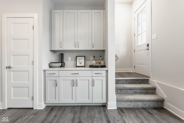 bar with baseboards, wood finished floors, a dry bar, and stairway