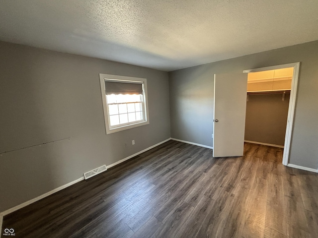 unfurnished bedroom with visible vents, a walk in closet, a textured ceiling, dark wood-style floors, and baseboards