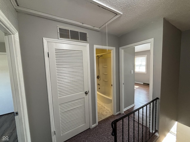 hallway with visible vents, an upstairs landing, a textured ceiling, baseboards, and attic access