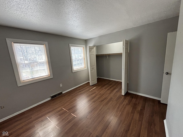 unfurnished bedroom with dark wood-style floors, visible vents, a closet, and baseboards