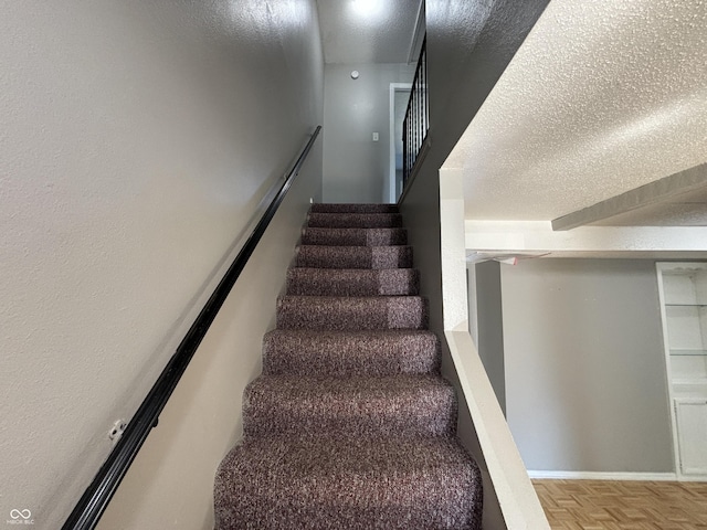 stairway with baseboards and a textured ceiling