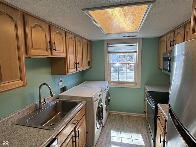 laundry area with a sink, light wood-style flooring, a textured ceiling, and washing machine and dryer