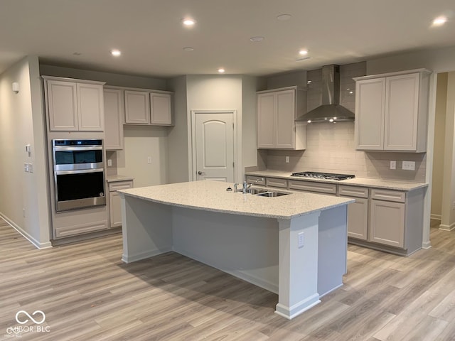 kitchen featuring light wood finished floors, appliances with stainless steel finishes, wall chimney range hood, and a sink