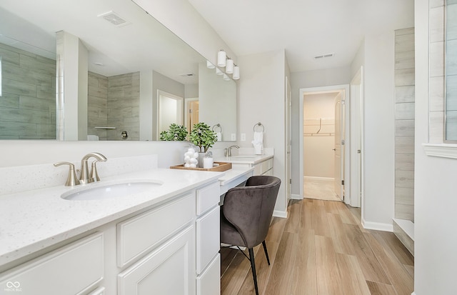 full bathroom featuring visible vents, a walk in shower, double vanity, wood finished floors, and a sink