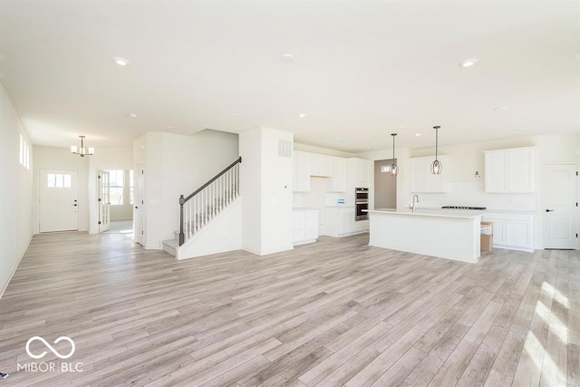 unfurnished living room featuring recessed lighting, stairway, light wood-style floors, and an inviting chandelier