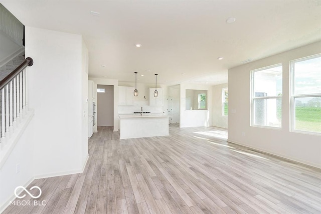 unfurnished living room with recessed lighting, baseboards, light wood-style floors, and a sink