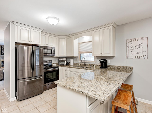 kitchen with a sink, stainless steel appliances, a peninsula, a breakfast bar area, and light stone countertops