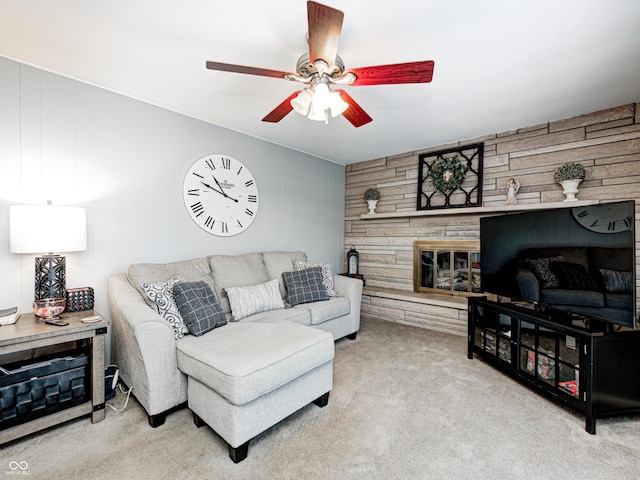 living area featuring wooden walls, a fireplace, ceiling fan, and carpet flooring