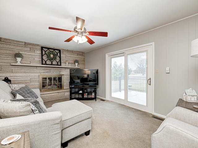 carpeted living area featuring visible vents, a stone fireplace, and ceiling fan