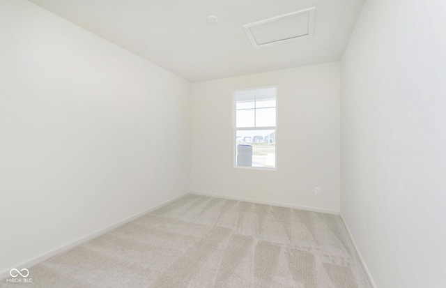 empty room with attic access, light colored carpet, and baseboards