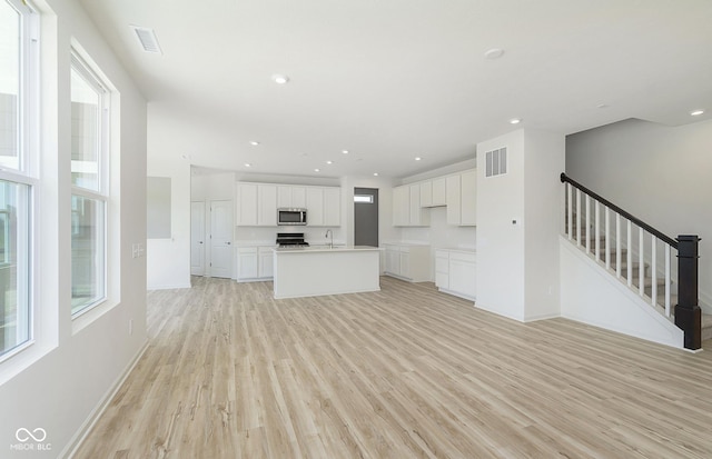 kitchen with stainless steel microwave, light wood-type flooring, visible vents, and a sink