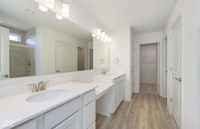 bathroom with visible vents, a walk in closet, a tile shower, wood finished floors, and vanity