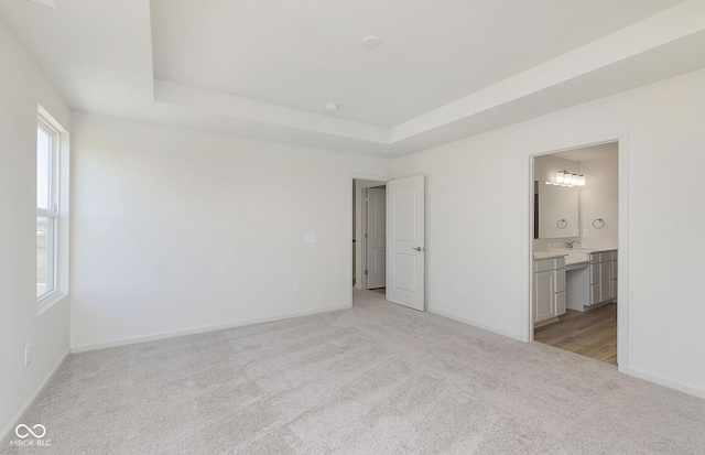 unfurnished bedroom with a tray ceiling, carpet, baseboards, and ensuite bathroom