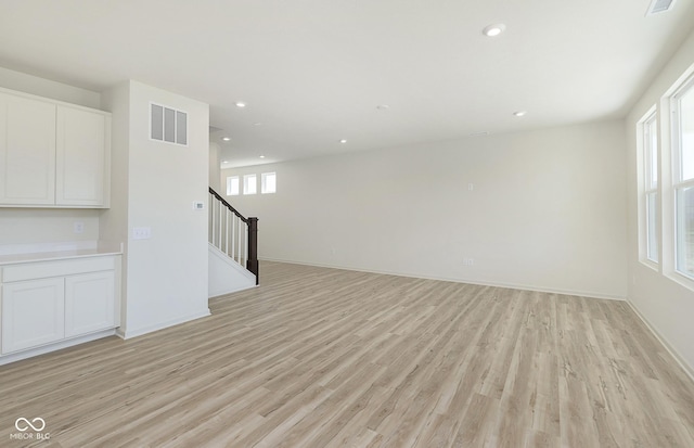 unfurnished living room with stairs, plenty of natural light, light wood-style floors, and visible vents