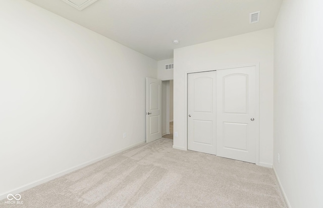 unfurnished bedroom with visible vents, light colored carpet, baseboards, and a closet