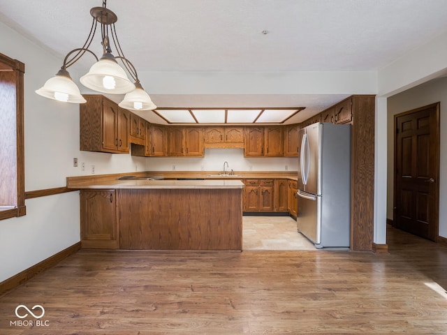 kitchen featuring a peninsula, freestanding refrigerator, light wood-style floors, and a sink